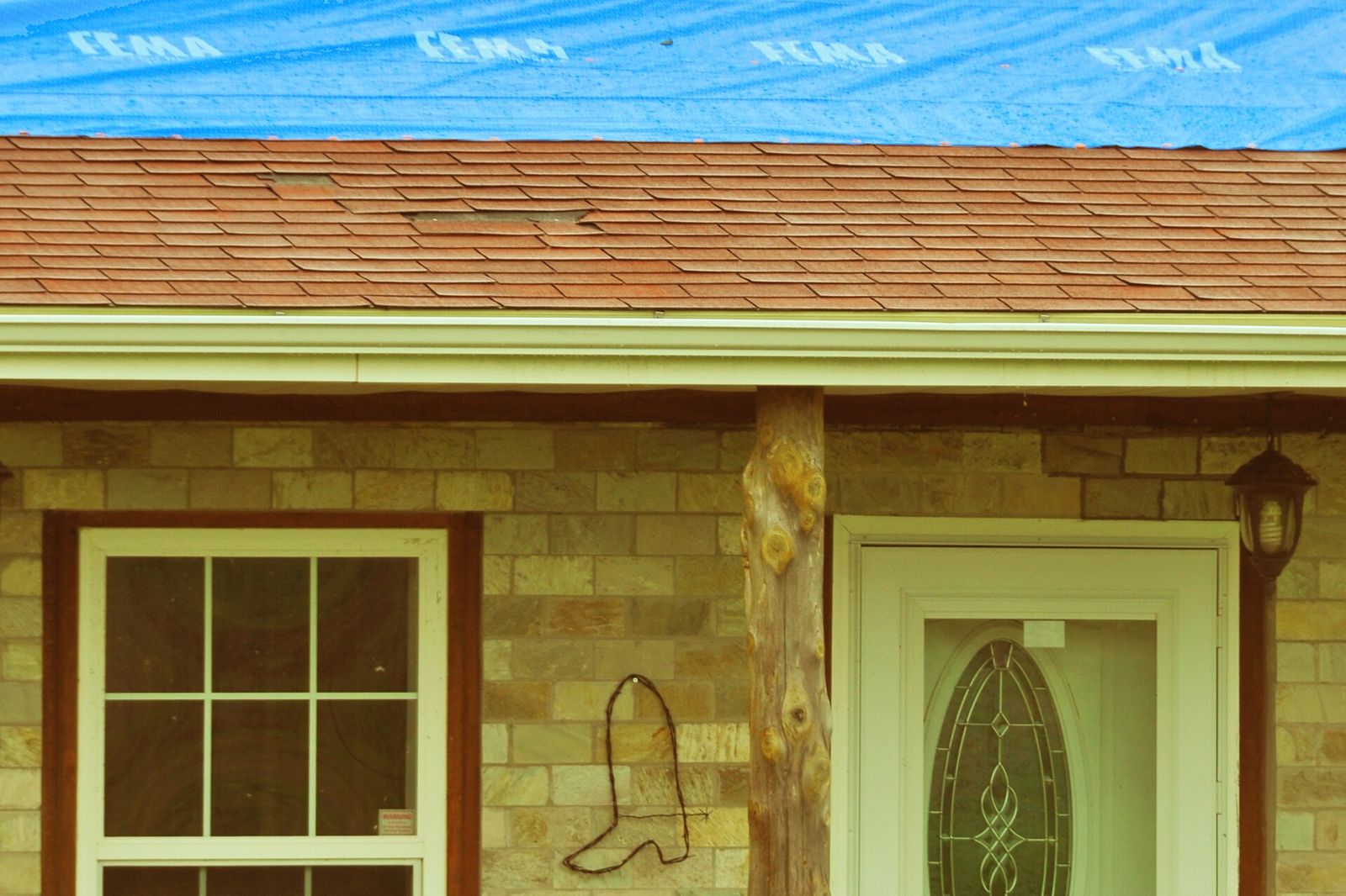 Close view of a blue tarp over missing shingles on a house roof